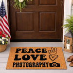 Peace Love Photography doormat featuring a retro font, a peace sign, a heart, and a camera icon on a natural coir welcome mat, displayed on a front porch with a flag and lantern for a stylish home entrance decor photography