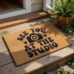 Photography studio doormat with a camera icon and the text See You At The Studio, this natural coir welcome mat features a durable fiber construction for front porch decor, perfect for photographers and creative business