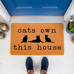 Cats Own This House doormat featuring black cat silhouettes on a natural coir fiber welcome mat, perfect for a funny pet lover front porch decor, durable outdoor floor rug for cat owners and feline themed home entryway entrance.
