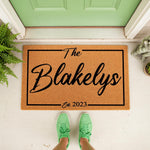 Personalized family name doormat featuring a custom last name and established year, this durable coir welcome mat sits on a porch as a stylish housewarming decor piece for your front door entrance and home entryway floor.