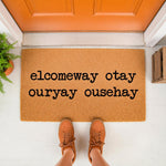 Funny welcome doormat with pig latin text on a natural coir fiber mat, placed at an orange front door entrance.