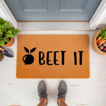 Beet It vegetable pun doormat featuring a black beet graphic on a natural coir welcome mat, perfect for a garden themed front porch decor, funny kitchen entry rug, or a unique housewarming gift for a gardener who loves vegetable