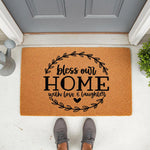 Bless Our Home doormat with love and laughter text, a natural coir welcome mat for front porch decor featuring a black leaf wreath design, perfect for housewarming entryways and outdoor floor mats to greet guests at your front