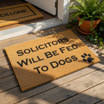 Funny dog lover doormat with the text Solicitors Will Be Fed To Dogs and a black paw print design, this natural coir fiber welcome mat is a humorous front porch decor piece for pet owners and dog house entrance floor mats.