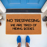 Funny doormat with text No Trespassing We Are Tired Of Hiding Bodies, a natural coir fiber welcome mat for front porch decor.