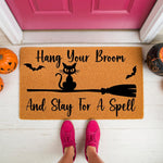 Halloween doormat with a black cat on a broomstick design, featuring the text Hang Your Broom And Stay For A Spell, this seasonal welcome mat is perfect for fall porch decor and spooky home entryway decorations for the holiday