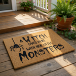 Witch Halloween doormat featuring a spider graphic and text that reads A Witch Lives Here With Her Little Monsters, this natural coir fiber welcome mat is a fun seasonal front porch decor piece for your home entrance.