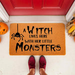 Witch Lives Here With Her Little Monsters doormat, a funny Halloween welcome mat for front porch decor featuring a spider graphic and spooky text on a natural fiber rug, perfect for seasonal home entryway and fall outdoor