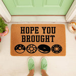 Donut welcome doormat with Hope You Brought text and donut icons on a natural coir fiber mat, placed at a front door entrance for a fun housewarming decor look that greets guests with a humorous food themed message for your home