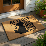 At least my dog loves me coir doormat featuring a black silhouette of a sitting puppy and heart accents on a natural fiber welcome mat, perfect for pet lovers looking for funny outdoor porch decor or a durable front door rug.