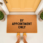 By Appointment Only doormat featuring bold black text on a natural coir fiber mat, placed at a yellow front door entrance to provide a funny, professional, and stylish welcome for visitors at your home or office porch entryway.