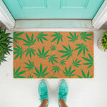 Marijuana leaf pattern coir doormat for front porch entryways, featuring a natural fiber welcome mat with green cannabis leaf prints, placed on a white floor in front of a teal door for a fun, casual home decor look.