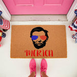 Patriotic coir doormat featuring a graphic of a bearded historical figure wearing flag-patterned sunglasses with the text Merica, perfect for a front porch welcome mat during summer holidays or for a rustic home entryway decor.