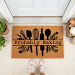Probably Baking kitchen doormat featuring black cooking utensil silhouettes and floral accents on a natural coir welcome mat, perfect for a baker home entrance or front porch decor for those who love to bake and cook in the