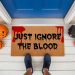 Scary Halloween doormat with Just Ignore The Blood text and red blood splatter design, this funny horror welcome mat is a perfect spooky porch decor piece for your front door entrance during the fall season and October holiday.