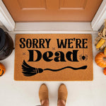 Sorry We're Dead Halloween doormat featuring a spooky broom and spider design on natural coir fiber, perfect for a front porch entryway during the fall season to welcome guests with funny holiday home decor and seasonal floor