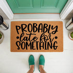Funny Probably Late For Something doormat featuring bold black text on a natural coir fiber mat, placed on a white porch in front of a green door, making a humorous welcome mat for a home entrance or a quirky housewarming gift