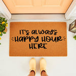 Happy Hour doormat for front porch entry, featuring a natural coir fiber welcome mat with black text that reads It's Always Happy Hour Here, placed on a white floor in front of a peach colored door with a lemon plant and lantern