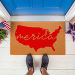 Patriotic USA map doormat featuring a red country silhouette and cursive text on natural coir fiber, perfect for a front porch welcome mat during summer holidays or Independence Day celebrations at a blue front door entrance.