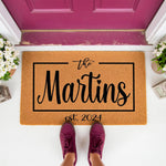 Personalized family name doormat featuring a custom last name and established year, this natural coir welcome mat sits on a front porch with a stylish script design, making it a durable outdoor floor rug for a new home entrance.