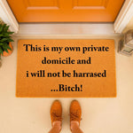Funny doormat with rude quote This is my own private domicile and i will not be harrased...Bitch! printed on a natural fiber welcome mat, placed on a porch in front of an orange door for a humorous home decor entryway statement