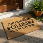 Funny dog doormat with the text The Dog Is In Charge We Just Live Here, featuring black paw prints on a natural coir fiber welcome mat, perfect for pet lovers looking for a humorous front porch rug or entryway floor decor.