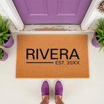 Personalized family name doormat featuring a custom last name and established year on natural coir fiber, perfect for a front porch entryway decor update, shown in a lifestyle setting with purple shoes and matching purple potted