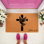Religious cross and dove doormat featuring a scripture verse, this natural coir welcome mat for front porch entryways displays a black cross with a flying dove design and the text John 3:16 for a faith-based home decor entrance.