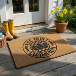Egg Hunt Champion coir doormat featuring a circular black design with a checkered pattern, three decorated Easter eggs, and leafy accents on a natural brown fiber background, perfect for a festive spring entryway or porch decor.