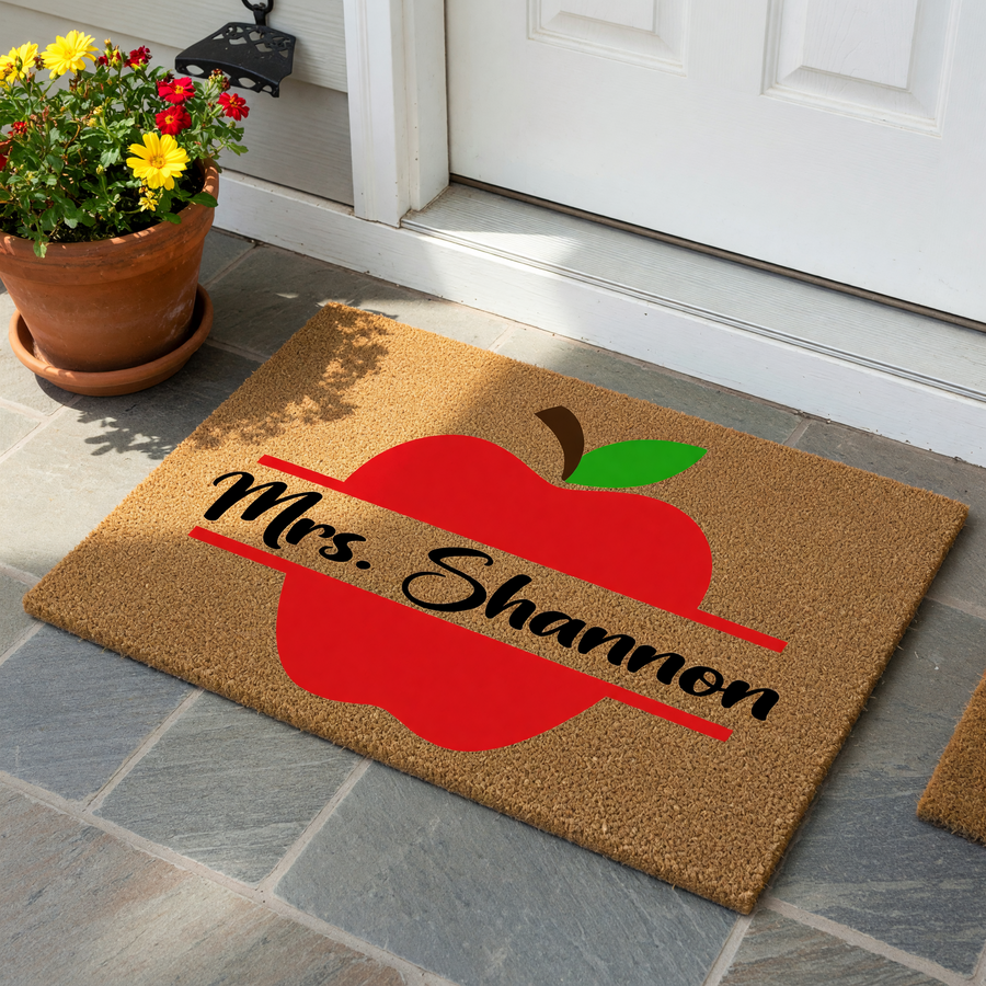 Personalized Teacher Apple Doormat featuring a large red apple graphic on a natural coir background, with a horizontal line design across the center for a custom name to be displayed in elegant black script lettering for a