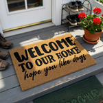 Funny Dog Lover Welcome Doormat featuring a natural coir texture with bold black lettering that reads Welcome To Our Home, hope you like dogs, making it a charming and humorous addition to any front porch or entryway for pet