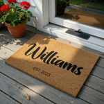 Personalized family name coir doormat featuring a natural brown textured surface with black script lettering for a last name and the established year printed below, creating a welcoming entrance decor piece for any modern home