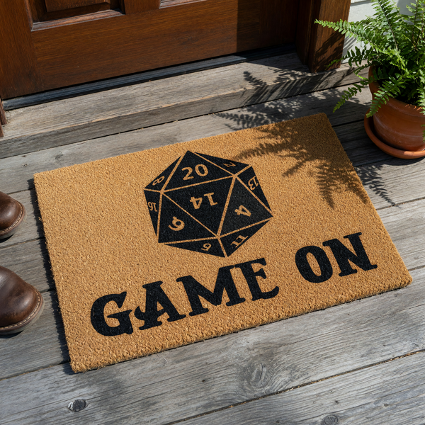 Dungeons and Dragons D20 doormat featuring a large black twenty-sided die graphic centered above the bold text Game On, printed on a natural brown coir fiber mat that is perfect for any gamer home entrance or tabletop gaming room.