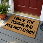 Funny Leave the Package and Back Away Slowly doormat featuring bold black text printed on a natural brown coir fiber mat, providing a humorous and functional welcome message for your front porch or entryway decor on a plain white