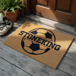 Personalized soccer ball doormat featuring a large black graphic of a soccer ball with a horizontal split across the center for a custom family name, set against a natural tan coir fiber background for a sporty outdoor entryway