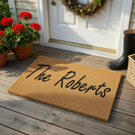 Personalized family name coir doormat featuring a natural tan fiber texture and bold black script lettering that displays a custom last name, providing a welcoming and durable entrance floor mat for any home front porch or