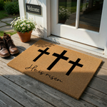 He Is Risen Easter Doormat featuring three black crosses printed on a natural tan coir fiber mat, creating a festive religious entryway decor piece that celebrates the spring holiday season with a clean and minimalist aesthetic.