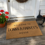 Personalized coir welcome doormat featuring a natural tan fiber texture and bold black lettering that reads Welcome To and House, with space in the center for a custom family name to create a warm entrance for any home front