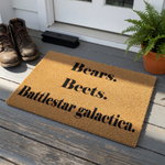 Funny TV show quote doormat featuring the text Bears, Beets, Battlestar Galactica printed on a natural coir fiber welcome mat, perfect for a front porch entry or home decor for fans of classic comedy television series and pop