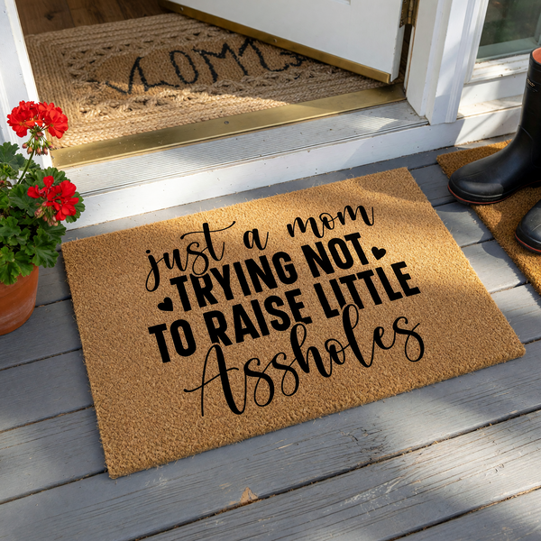 Funny Mom Doormat featuring a natural coir texture with bold black typography that reads just a mom trying not to raise little assholes, creating a humorous and relatable welcome mat for any front porch or entryway home decor.