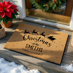 Personalized Christmas doormat featuring a black silhouette of Santa and his reindeer flying across a natural coir fiber mat, with festive text that reads Christmas at the Smiths and a decorative flourish on a plain white