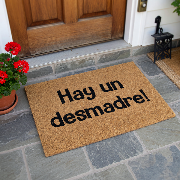Funny Spanish doormat featuring the phrase Hay un desmadre printed in bold black letters on a natural tan coir fiber background, creating a humorous and welcoming entrance piece for any home entryway or front porch decor.