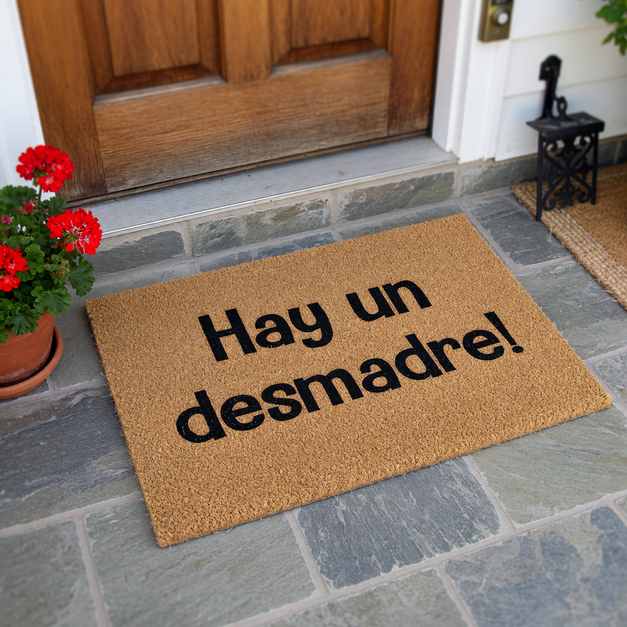 Funny Spanish doormat featuring the phrase Hay un desmadre printed in bold black letters on a natural tan coir fiber background, creating a humorous and welcoming entrance piece for any home entryway or front porch decor.