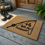 Fishing themed coir doormat featuring a black graphic of a fishing rod and line with the humorous text Oh bite me printed in a stylish script font, set against a natural tan textured fiber background for a rustic outdoor entryway.