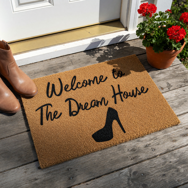 a textured area rug with the text "Welcome to The Dream House" printed on it, along with a silhouette of a high-heeled shoe.