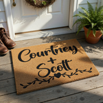 Personalized couple doormat featuring a natural coir texture with black script lettering and a decorative vine and heart design, providing a welcoming touch for a front porch entrance while showcasing a custom name design for new