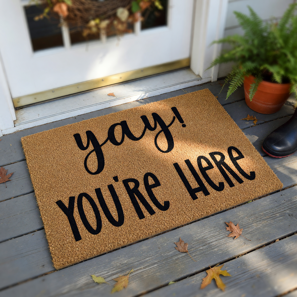 Yay You're Here coir doormat featuring a natural brown fiber texture and bold black lettering, designed as a welcoming front porch entrance mat to greet guests at your home with a cheerful and friendly message for visitors.