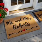 Personalized Mr. and Mrs. coir doormat featuring a natural tan fiber texture with black script lettering and a small red heart accent, providing a welcoming touch for a newlywed couple's front porch entrance on a clean white
