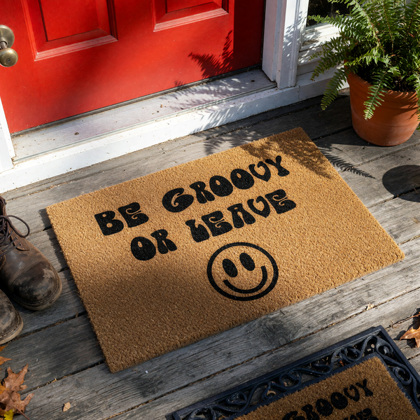 Be Groovy or Leave coir doormat featuring a retro-inspired font and a large black smiley face icon, set against a plain white background to highlight the natural tan texture of the durable outdoor welcome mat for a fun home