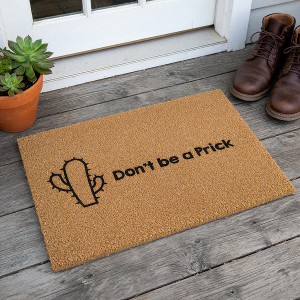 Funny Cactus Welcome Doormat featuring a natural coir texture and a bold black graphic of a prickly cactus, accompanied by the humorous text Don't be a Prick printed in a clean, modern font on a plain white studio background.